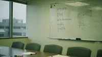 A Canadian boardroom whiteboard with hand-written attack types listed in a column defacement DDoS data tampering and graffiti in blue marker