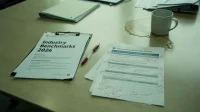 A printed industry benchmarks document on a Canadian conference table beside a cyber-insurance renewal questionnaire with handwritten margin notes
