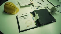 A black binder labelled co-managed IT runbook open on a Canadian construction-firm conference table with tabs labelled by responsibility split and a hard hat in the background