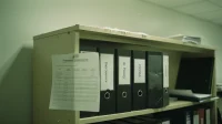 A Canadian office bookshelf with binders labelled data governance AI policy PIPEDA along the spines and a printed crosswalk paper-clipped to one