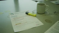 A printed phishing awareness training handout on a Canadian conference table with red-pen circles around suspicious URLs and a coffee mug