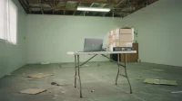 Nearly empty Canadian startup warehouse office with a folding table, closed laptop and a stack of unboxed equipment