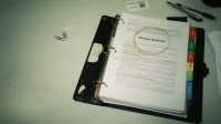 Printed startup IT runbook open in a binder on a Canadian shared workspace table beside sticky notes