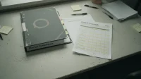 A binder labelled startup compliance open on a Canadian shared workspace table beside a printed PIPEDA crosswalk and a coffee mug with a ring stain