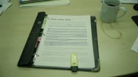 A printed Voice of the CISO report in a binder open on a Canadian conference table with a yellow highlighter and a coffee mug with a ring stain
