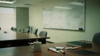 A Canadian boardroom whiteboard with a hand-drawn roadmap of growth milestones in blue marker beside a row of empty chairs and a coffee mug